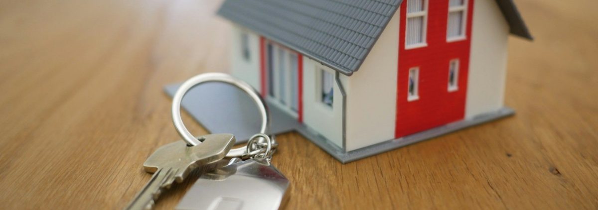 A tiny model of a white and red New Hampshire Seacoast home sits next to a set of keys on a table