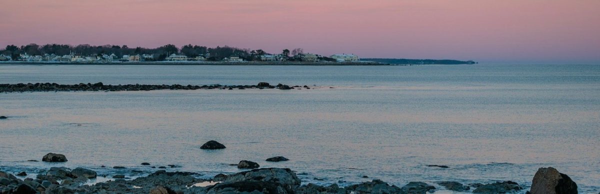 Buying a New Hampshire seacoast home: a purple and orange sunset unfolds over a rocky coastline near Rye, New Hampshire.